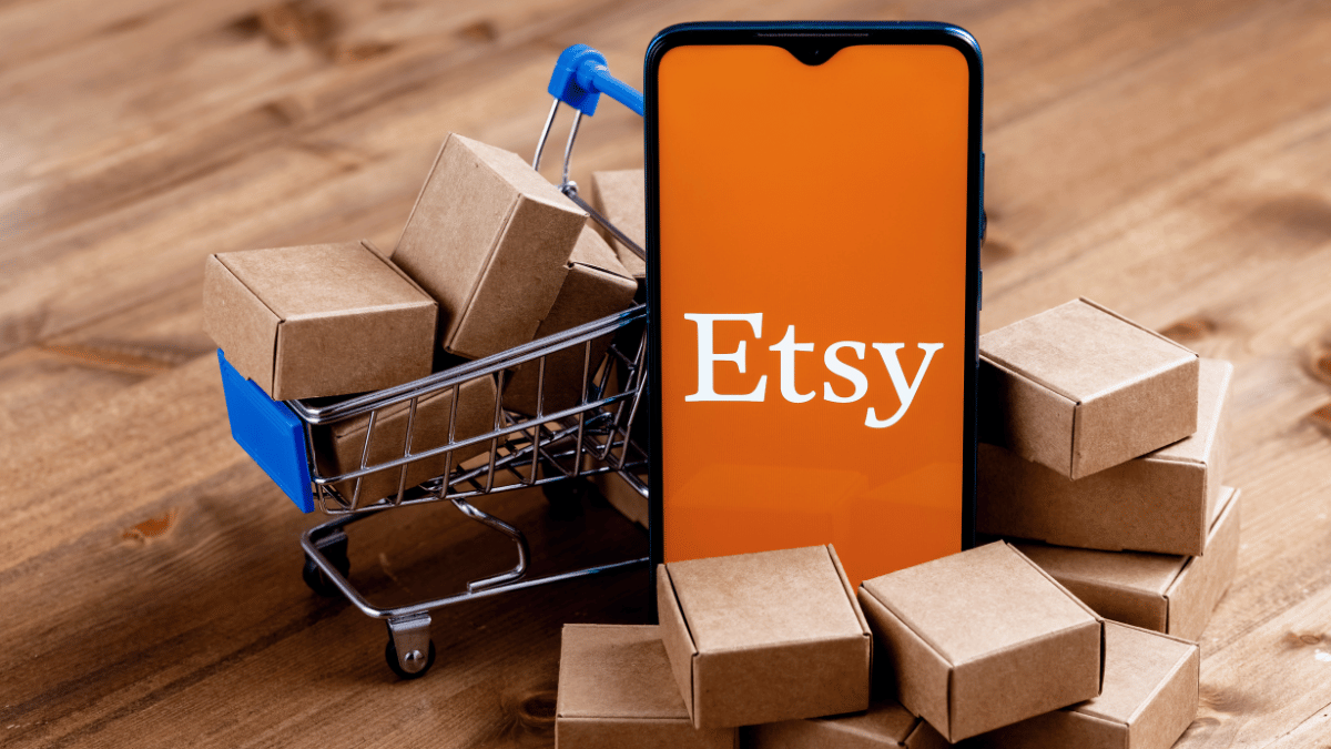 Image of a phone with an Etsy logo on it in front of boxes and a shopping trolley